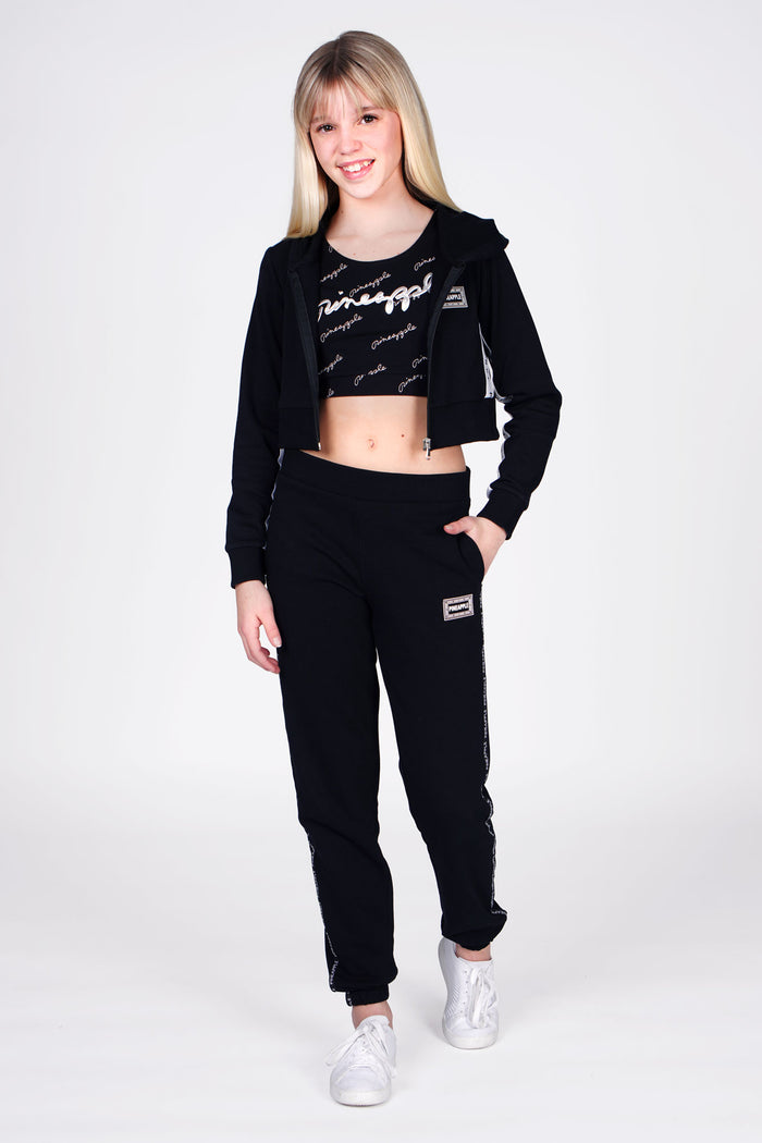 Girl wearing Black Tape Joggers with white stripe, and Black Tape Zip Hoodie and Black All Over Print Crop Top, full side view