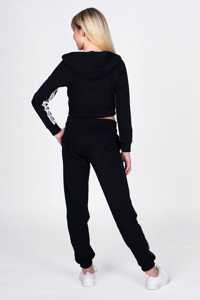 Girl wearing Black Tape Joggers with white stripe, and Black Tape Zip Hoodie, full back view