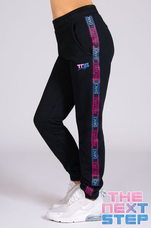 Black joggers with pockets featuring Pineapple x The Next Step tape and branded logo on the left leg.