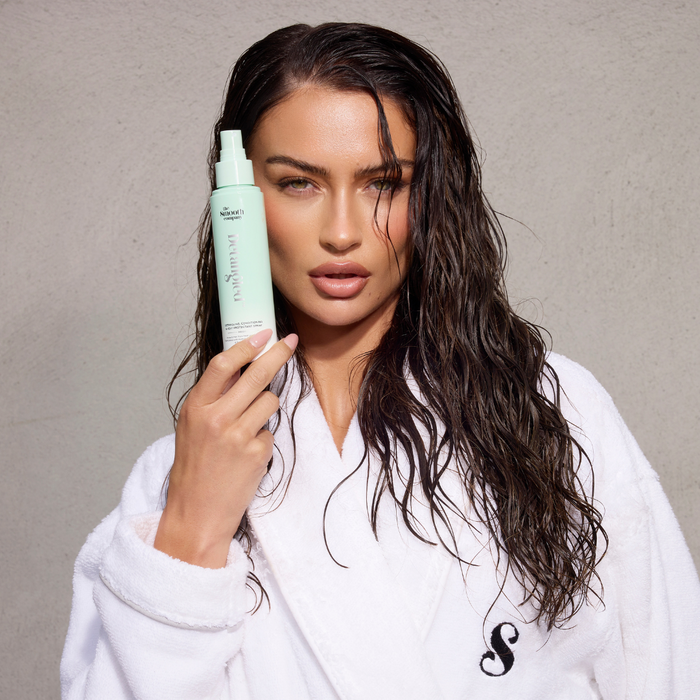 Woman holding a bottle of hair care product against a neutral background