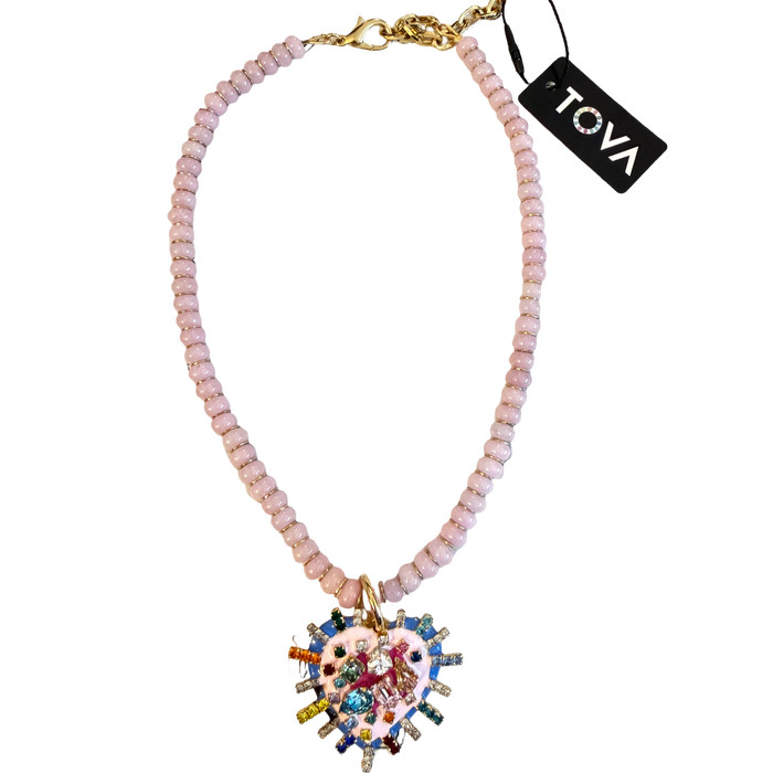A Tova brand beaded necklace featuring light pink faceted beads, a gold-tone clasp, and a large, colorful heart-shaped pendant with cartoon-style illustrations and rhinestones.