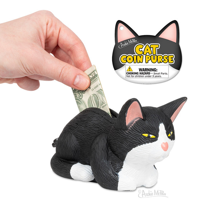 A hand placing a dollar bill into the Tuxedo Cat Coin Purse, featuring an attached warning label.