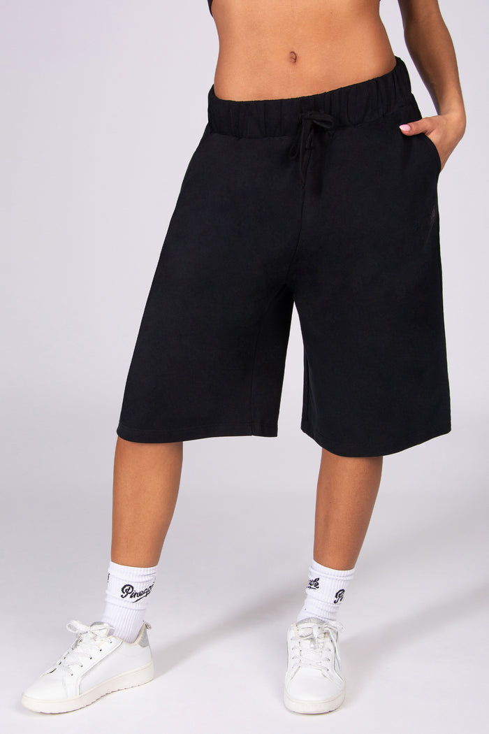 Black super oversized basketball shorts worn by a person on a white background