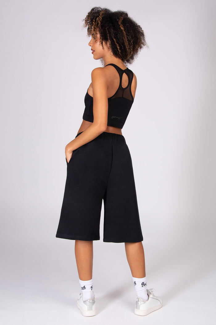 Woman wearing a black crop top and black super oversized basketball shorts  on a light grey background