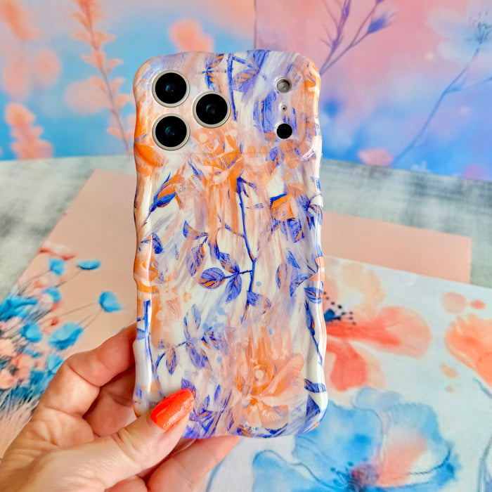 Hand holding the Where Dreams Bloom Wavy Luxe MagSafe iPhone case, showing the watercolor floral print in periwinkle, peach and coral.