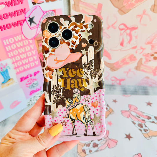 Hand holding the Yee Haw Honey Wavy Luxe MagSafe iPhone case, showing the brown cow print with a horse, cactus and Yee Haw lettering over a pink floral base.
